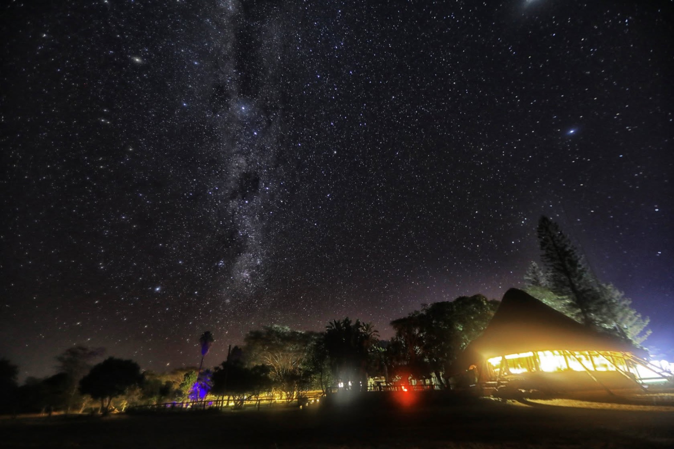 Milky Way over a lit thatch lodge